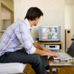 mezczyzna oglada telewizje i pracuje na laptopie